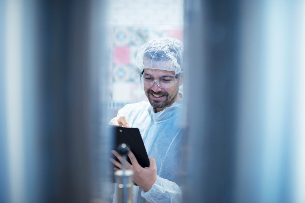 Technologue professionnel en combinaison de protection blanche contrôlant la production et rédigeant les résultats dans une usine alimentaire.