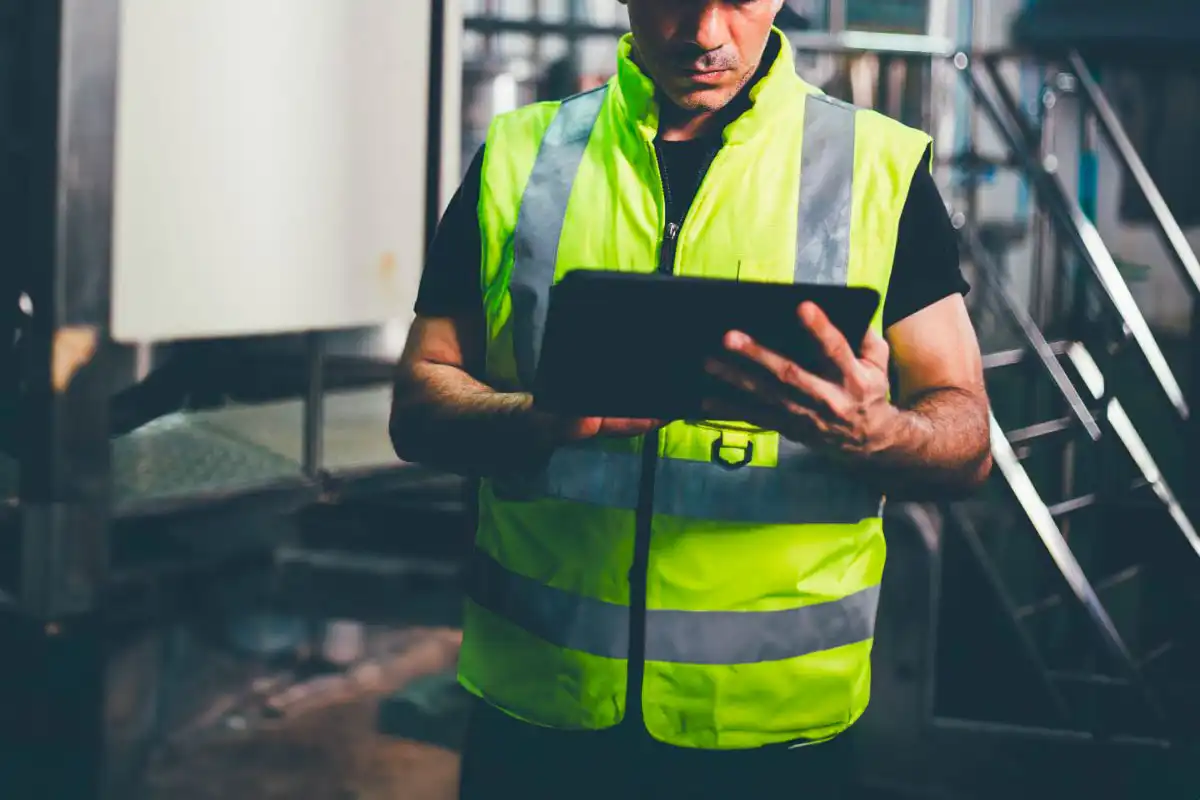 Technicien industriel utilisant une tablette pour gérer la maintenance assistée par ordinateur (GMAO) dans un environnement de production.