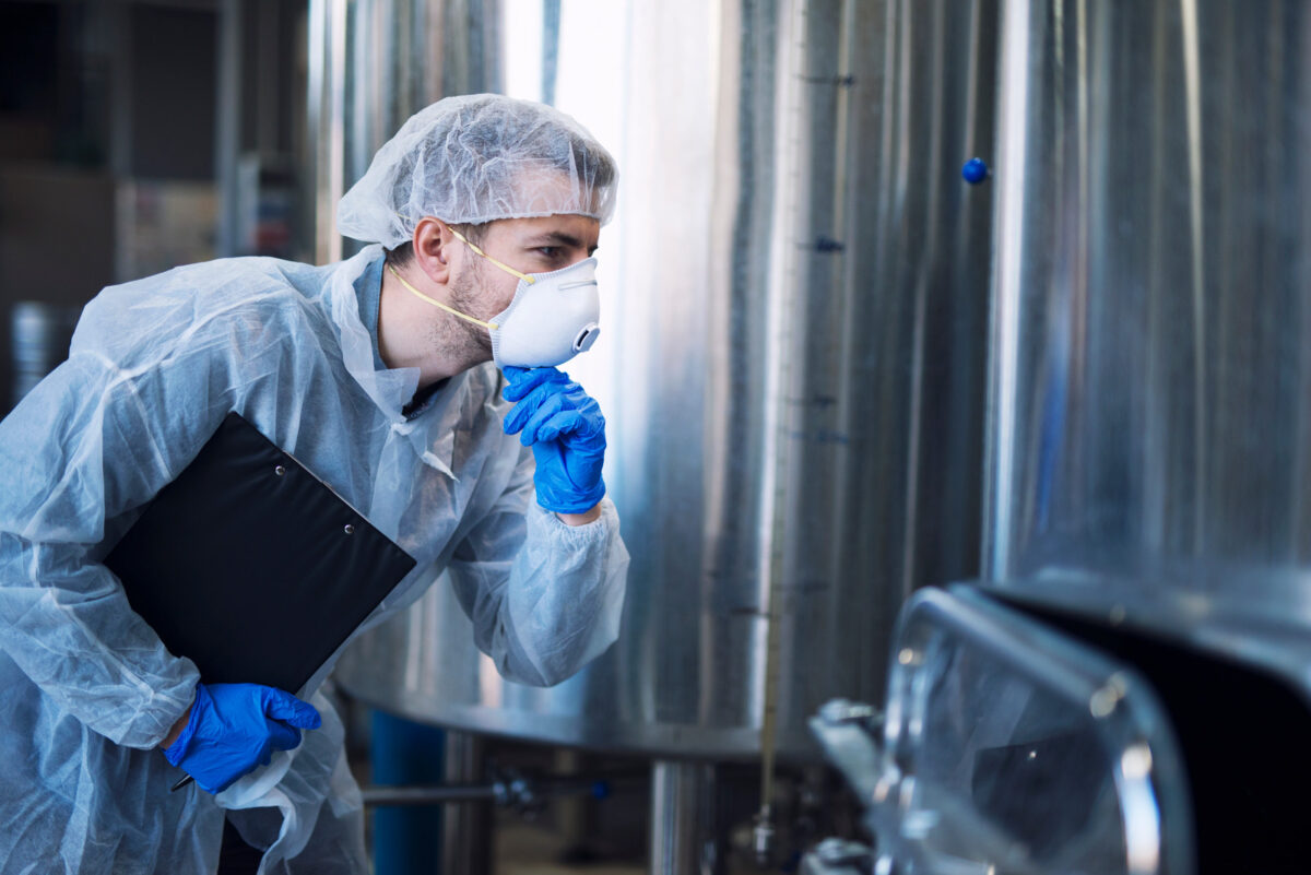 Ouvrier d'usine en uniforme de protection blanc avec filet à cheveux et masque, regardant les paramètres d'une machine industrielle.