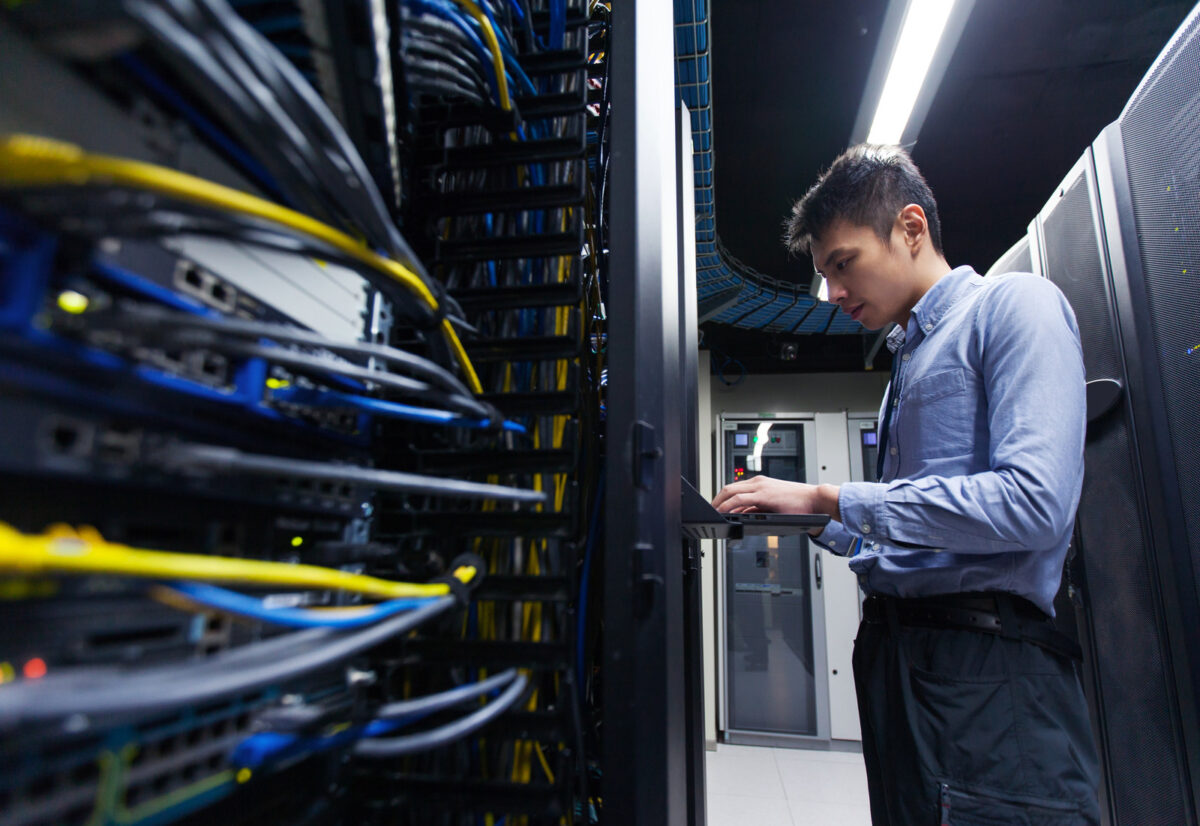 Jeune ingénieur informatique inspectant les serveurs d'un centre de données.